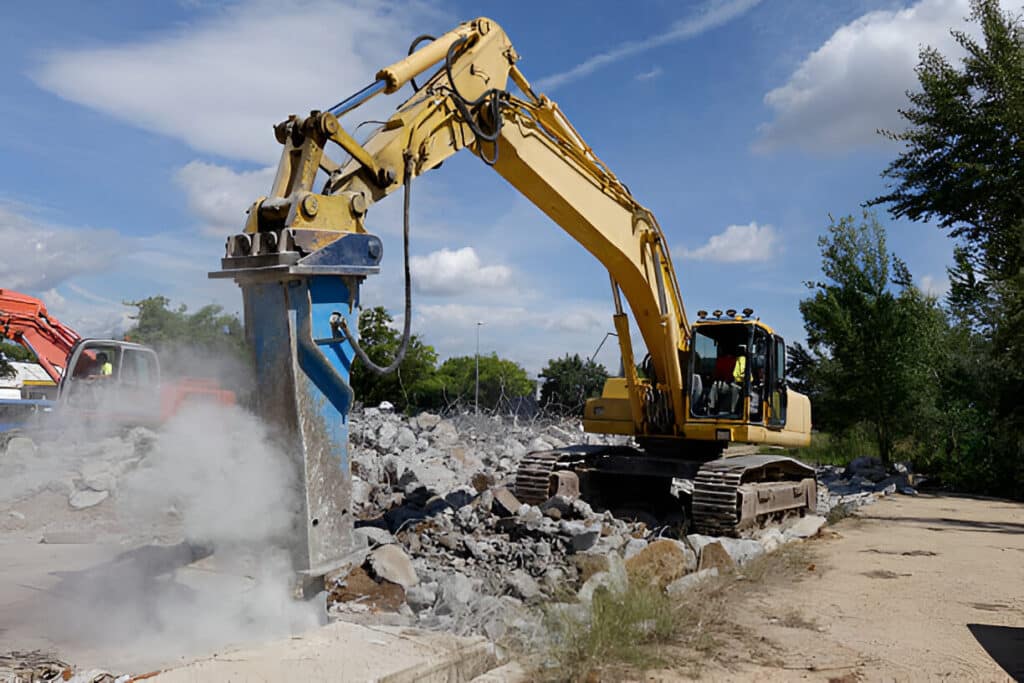 Hydraulic rock breaker attachment mounted on the arm of an excavator on an Indian site